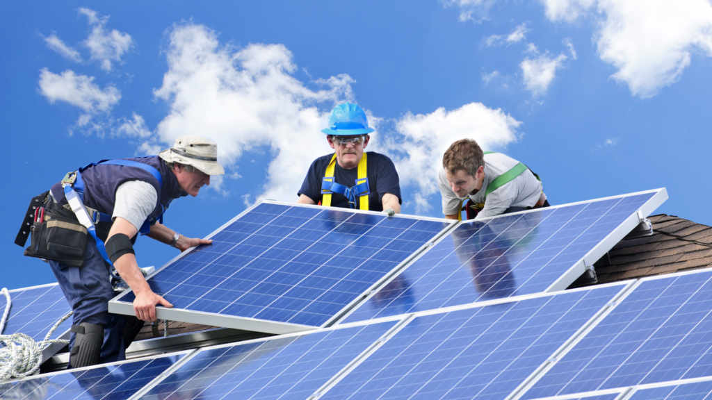 Three men installing solar panels on a roof.