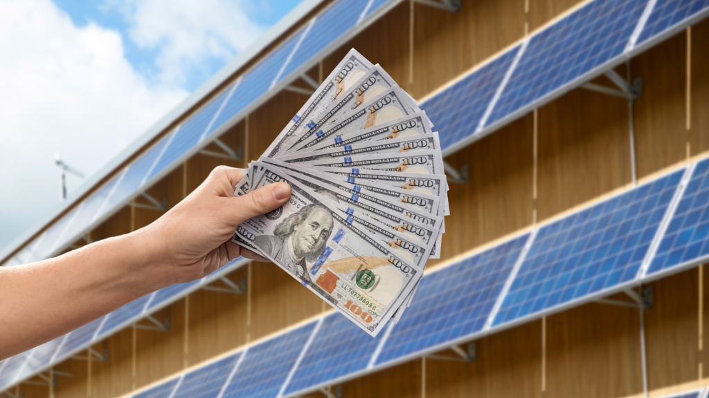 A hand holding a stack of money in front of solar panels, depicting financial gains from renewable energy.