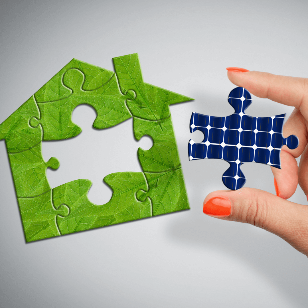 A person holding a puzzle piece with a green house and solar panels.