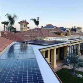 Aerial view of a residential property with solar panels installed on one of the roofs, featuring a spanish-style architecture with terracotta tiles and a landscaped garden.