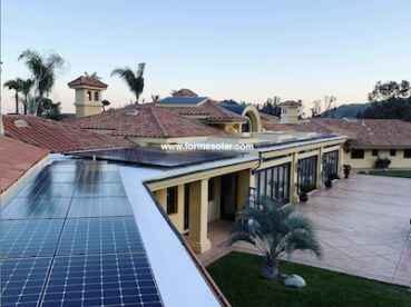 Aerial view of a large suburban home with a tile roof, featuring solar panels on one section, during sunset.